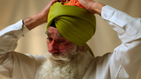 Primer-Plano-De-Estudio-De-Un-Hombre-Sikh-Mayor-Con-Barba-Atando-Tela-Para-Un-Turbante-Contra-Un-Fondo-Liso,-Filmado-En-Tiempo-Real-1